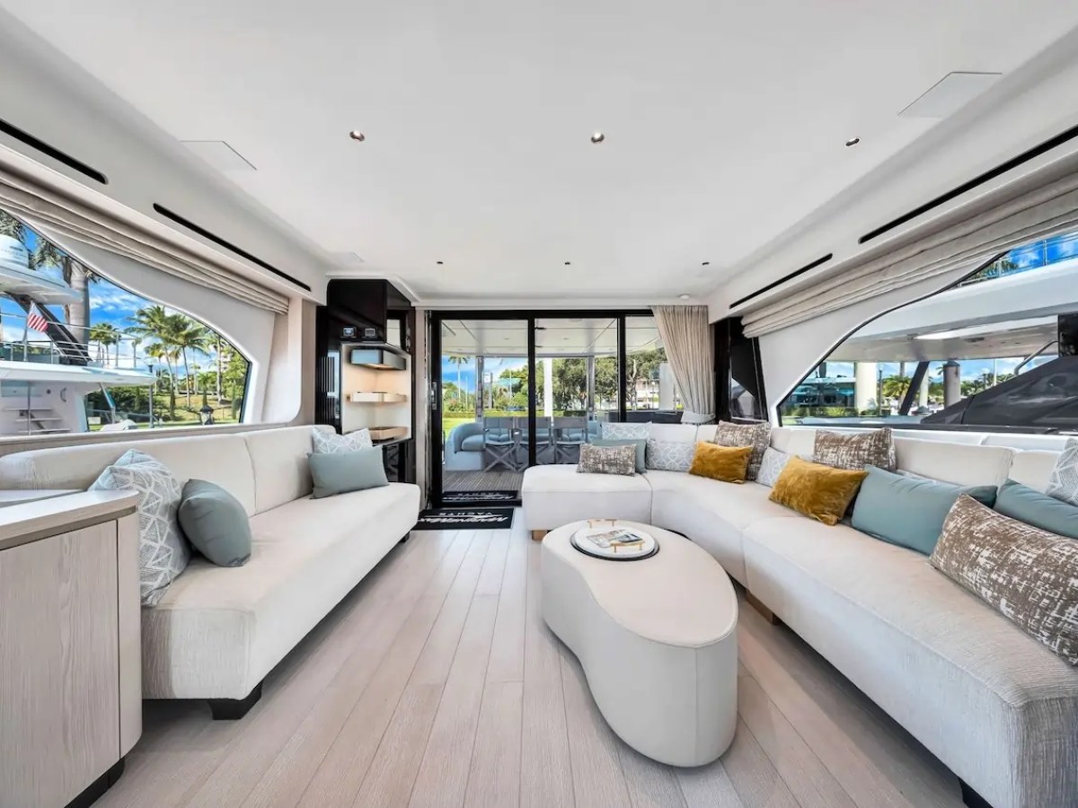 Spacious yacht interior with beige sofas, large windows, and decorative cushions.