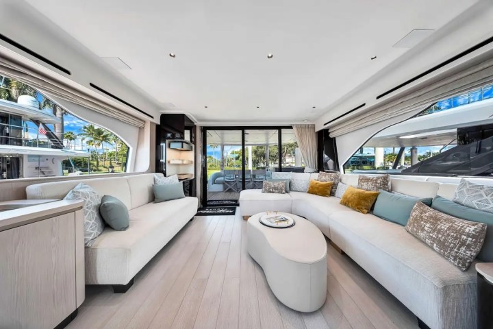 Spacious yacht interior with beige sofas, large windows, and decorative cushions.