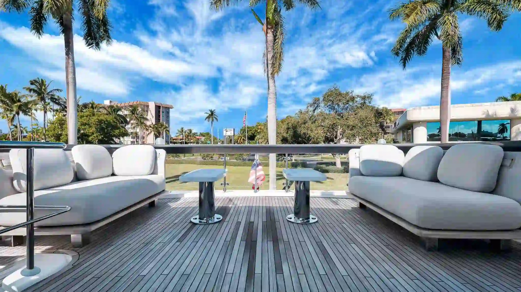 Outdoor deck with two plush sofas, palm trees, and a clear blue sky.
