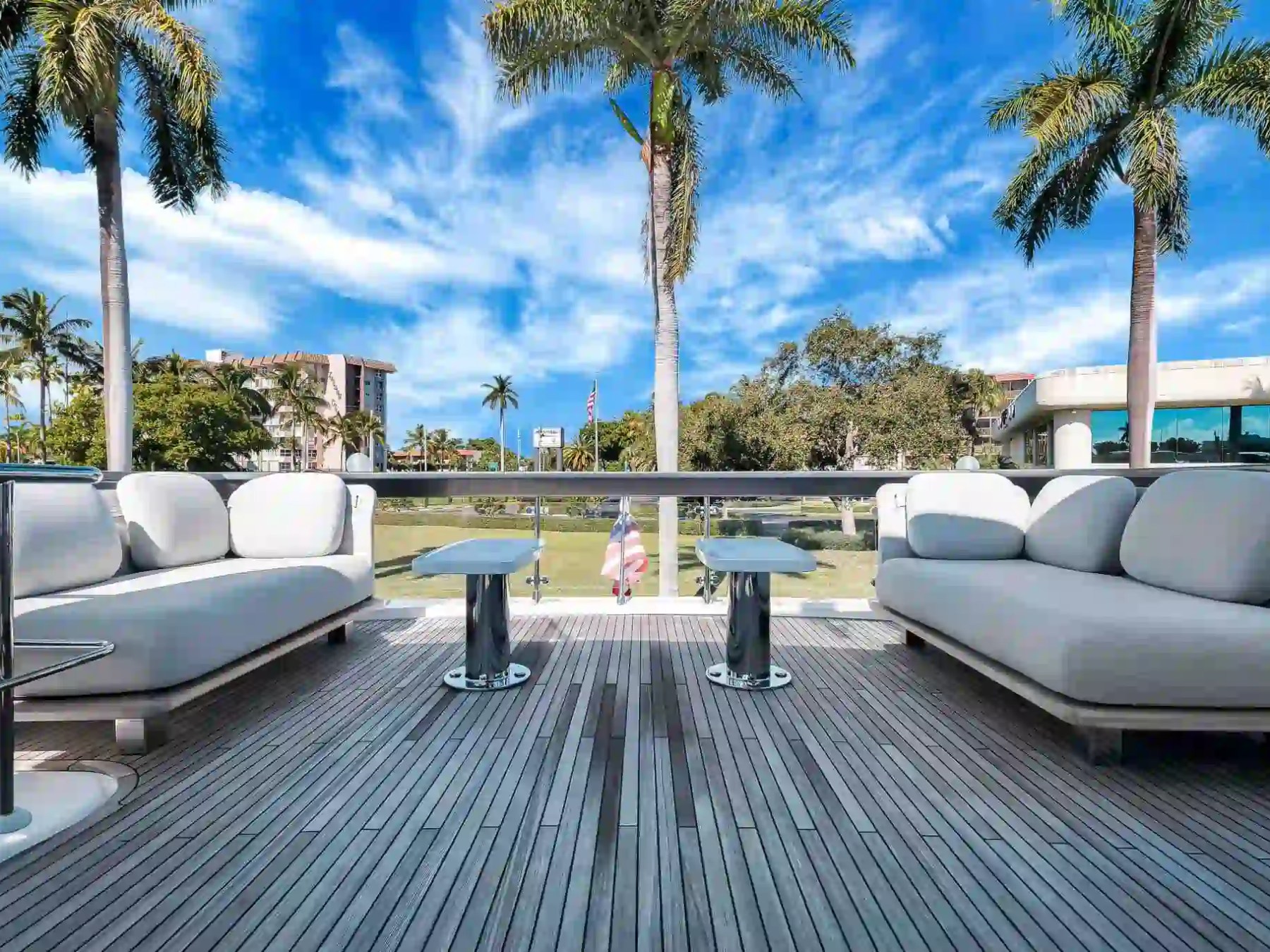 Outdoor deck with two plush sofas, palm trees, and a clear blue sky.