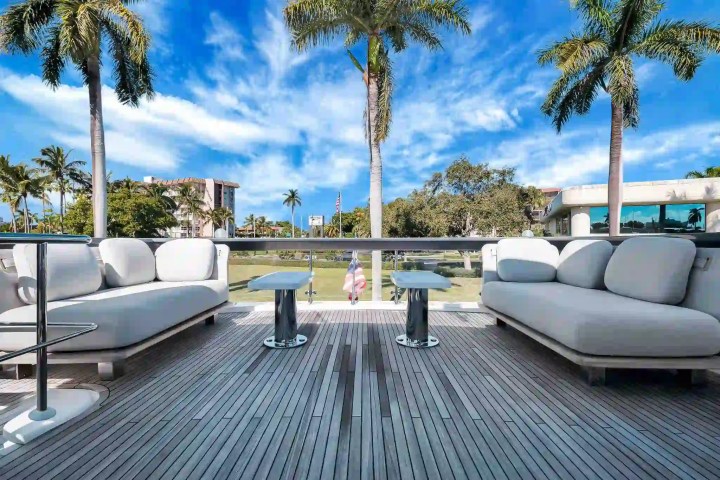 Outdoor deck with two plush sofas, palm trees, and a clear blue sky.