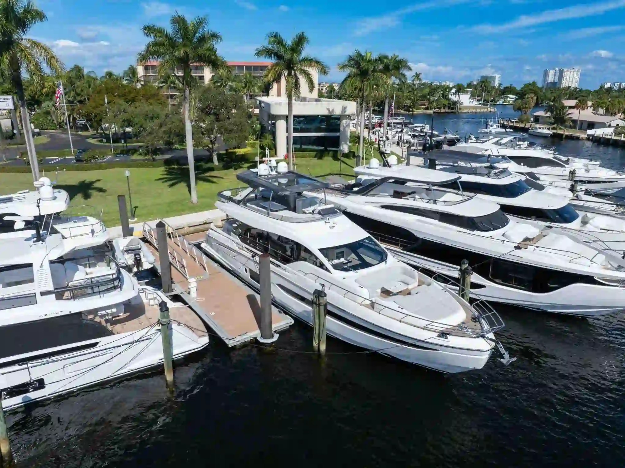 Luxury yachts docked at a marina, surrounded by palm trees and green landscape.
