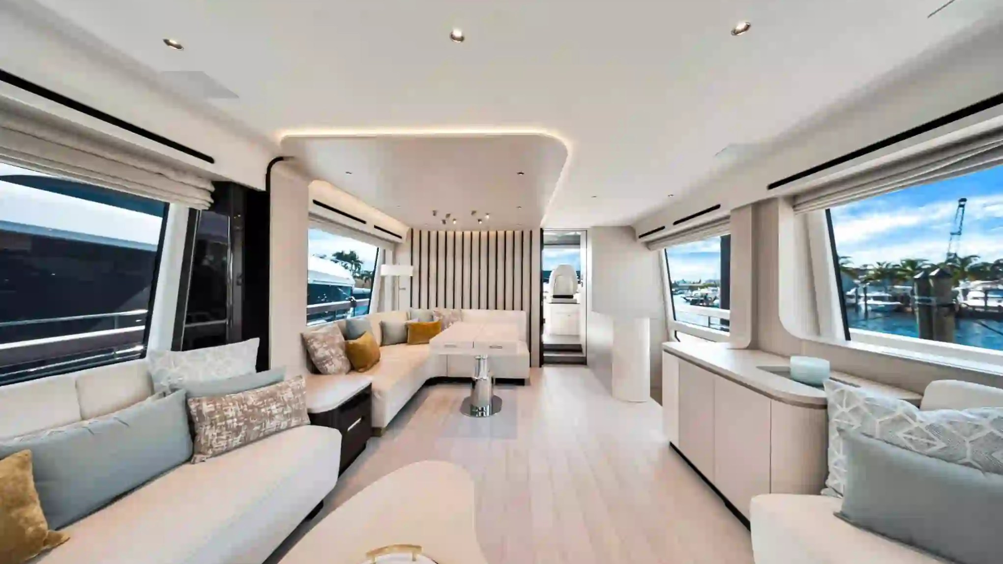 Luxurious boat interior with white seating, large windows, and a view of a marina outside.
