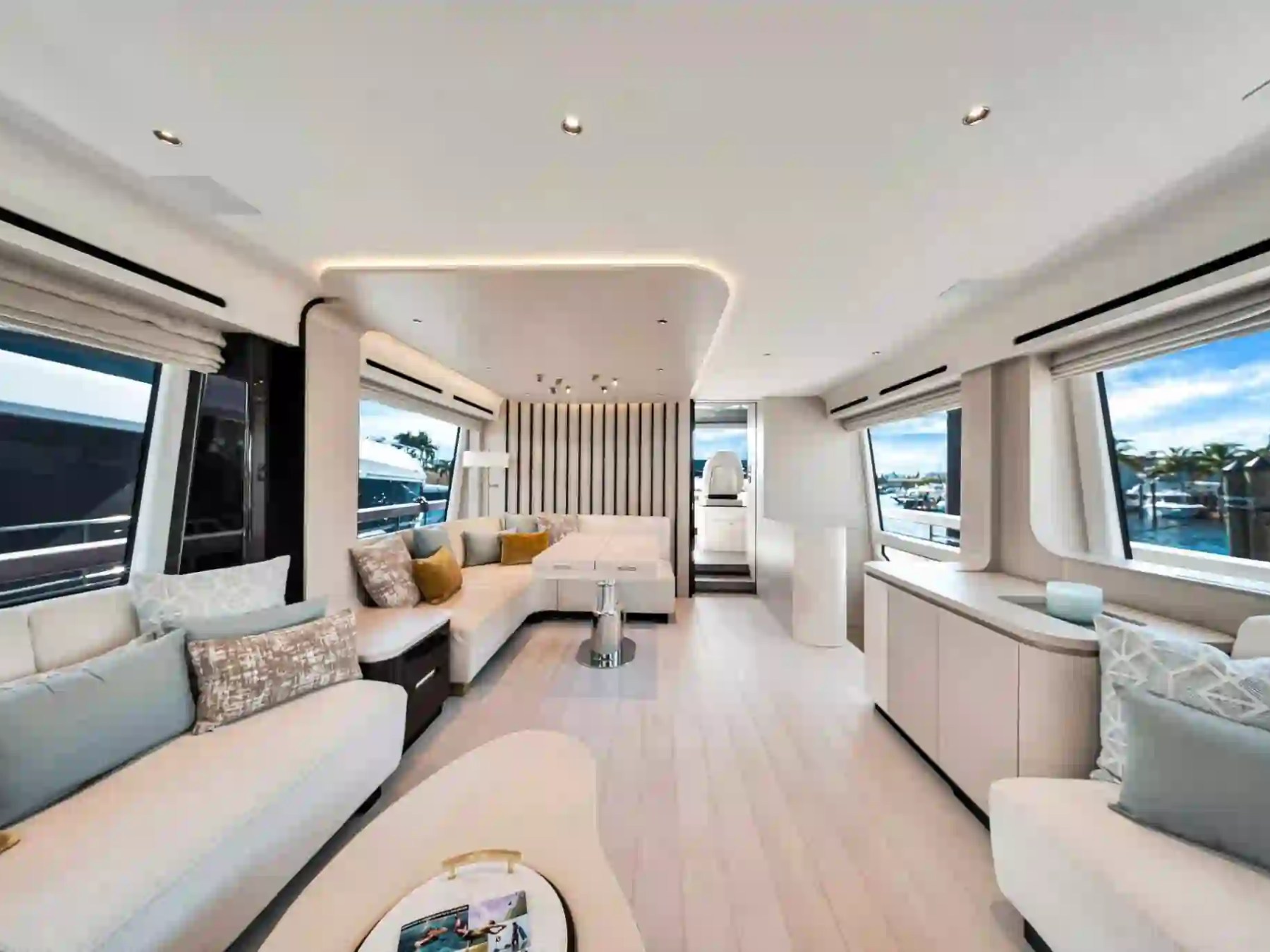 Luxurious boat interior with white seating, large windows, and a view of a marina outside.