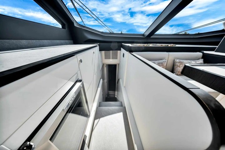 Interior of a modern boat with sleek white cabinetry, a small fridge, and large window with view of blue sky.