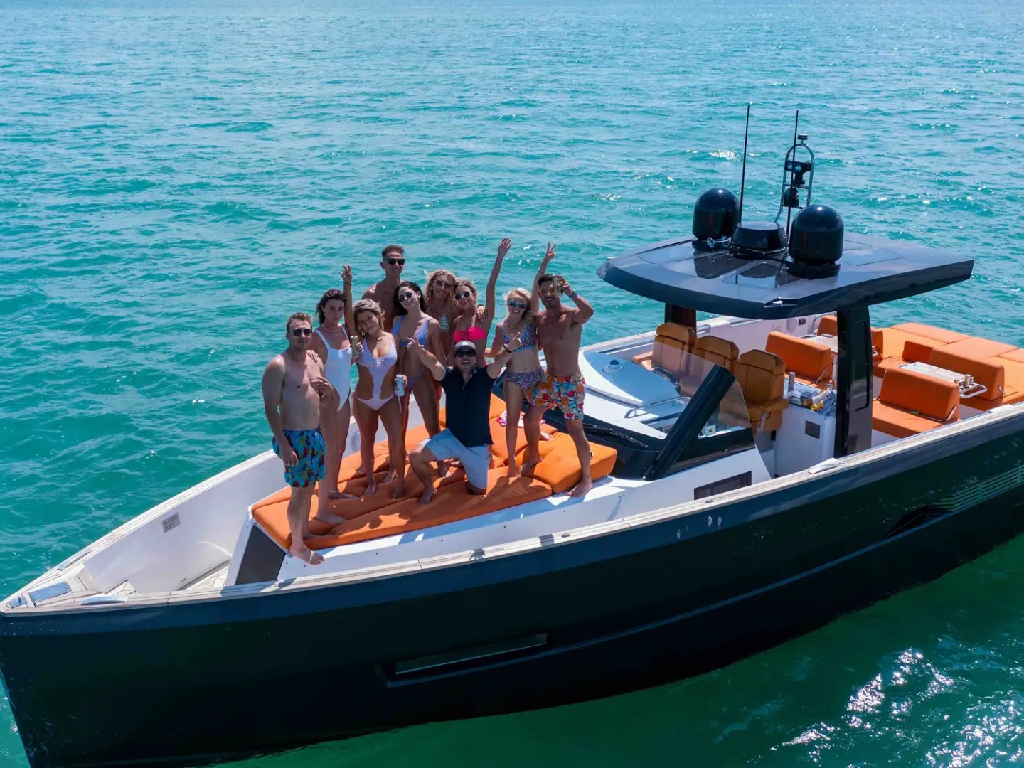 People celebrating on a black boat with orange seats in clear blue water.
