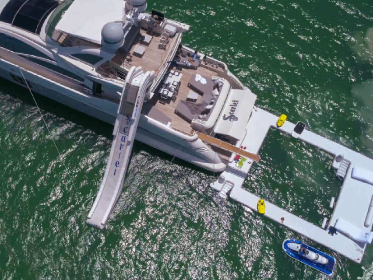 Luxury yacht with water slide and floating dock on green water.