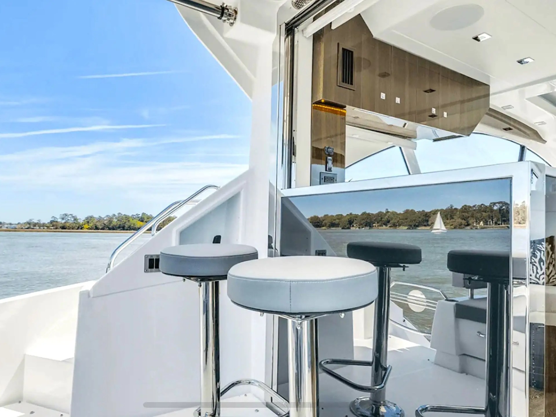 Yacht interior with bar stools and mirrored surfaces, overlooking water and trees.