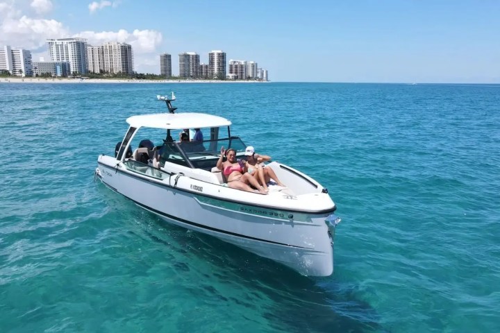 People relaxing on a boat in blue ocean near city skyline in the background.