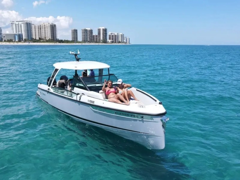 People relaxing on a boat in blue ocean near city skyline in the background.