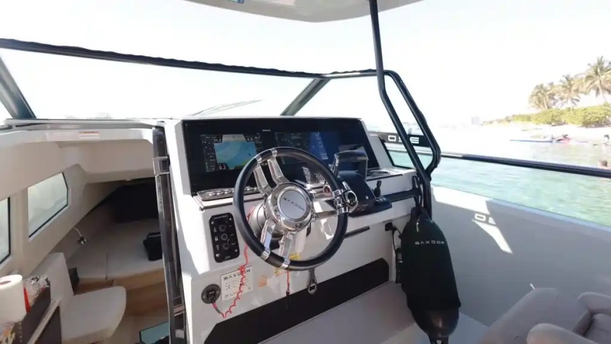 Boat cockpit with steering wheel, control panel, and cabin view.