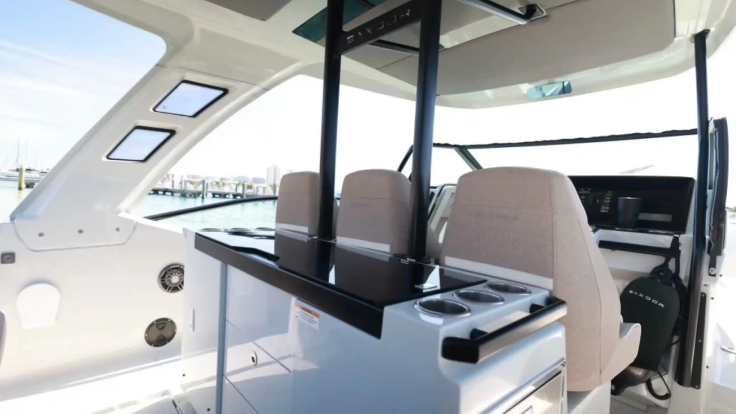 Interior of a modern boat with beige seats, black countertop, and windows showing a dock view.