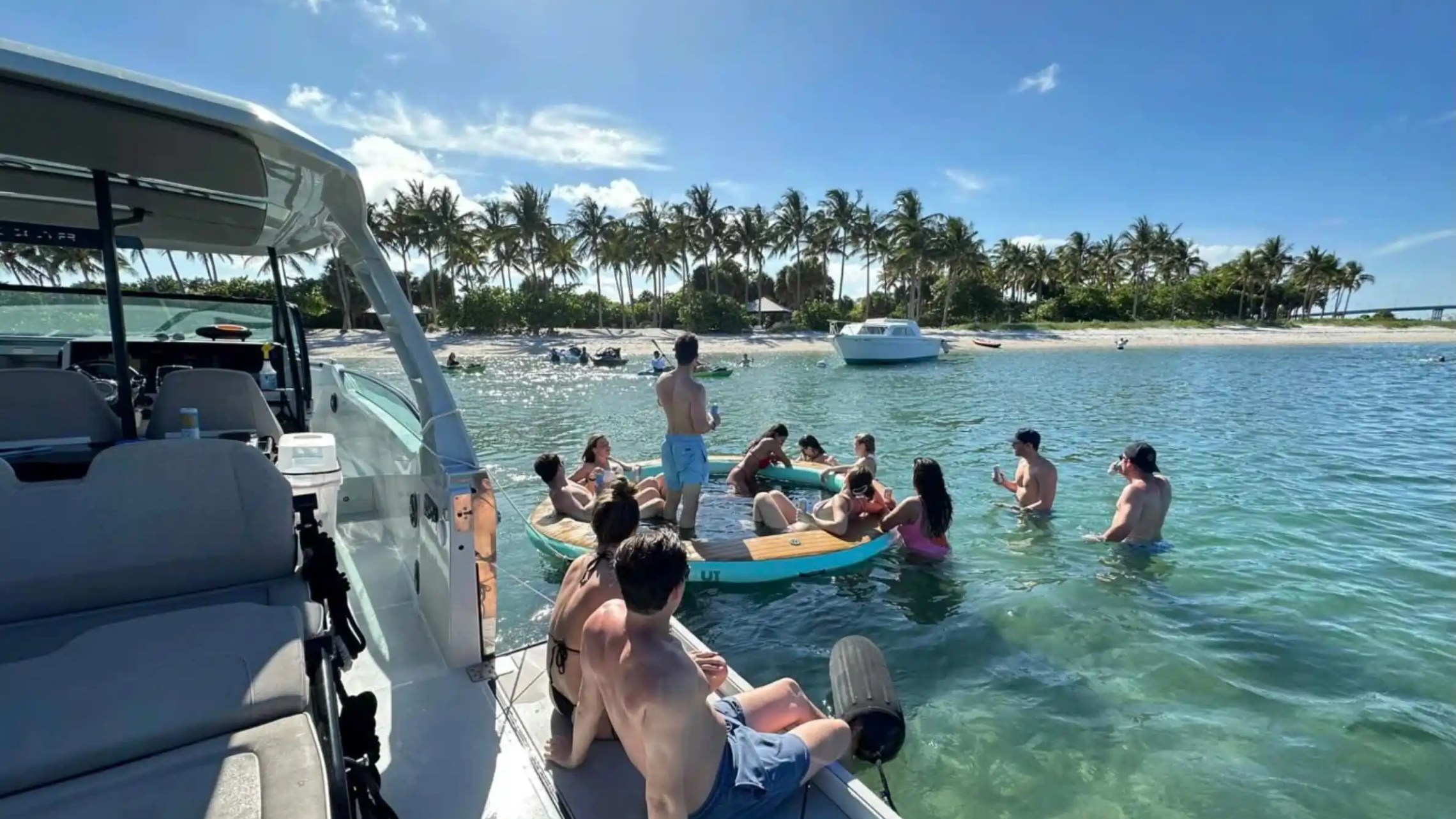 Group of people relaxing on a float and boat near tropical beach with palm trees.