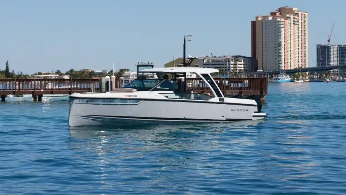 A motorboat cruising on calm water near a cityscape with buildings and a bridge in the background.