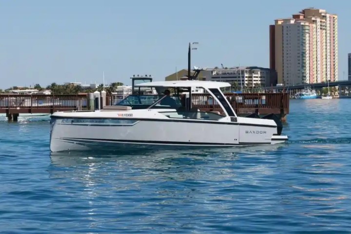 A motorboat cruising on calm water near a cityscape with buildings and a bridge in the background.