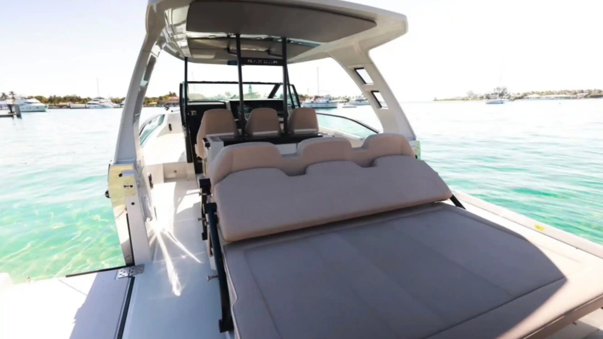 Luxury boat with beige seating and canopy, docked on turquoise water.