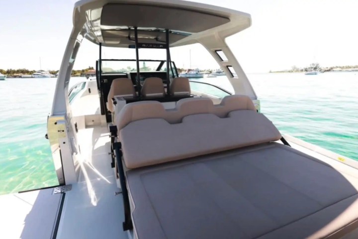 Luxury boat with beige seating and canopy, docked on turquoise water.
