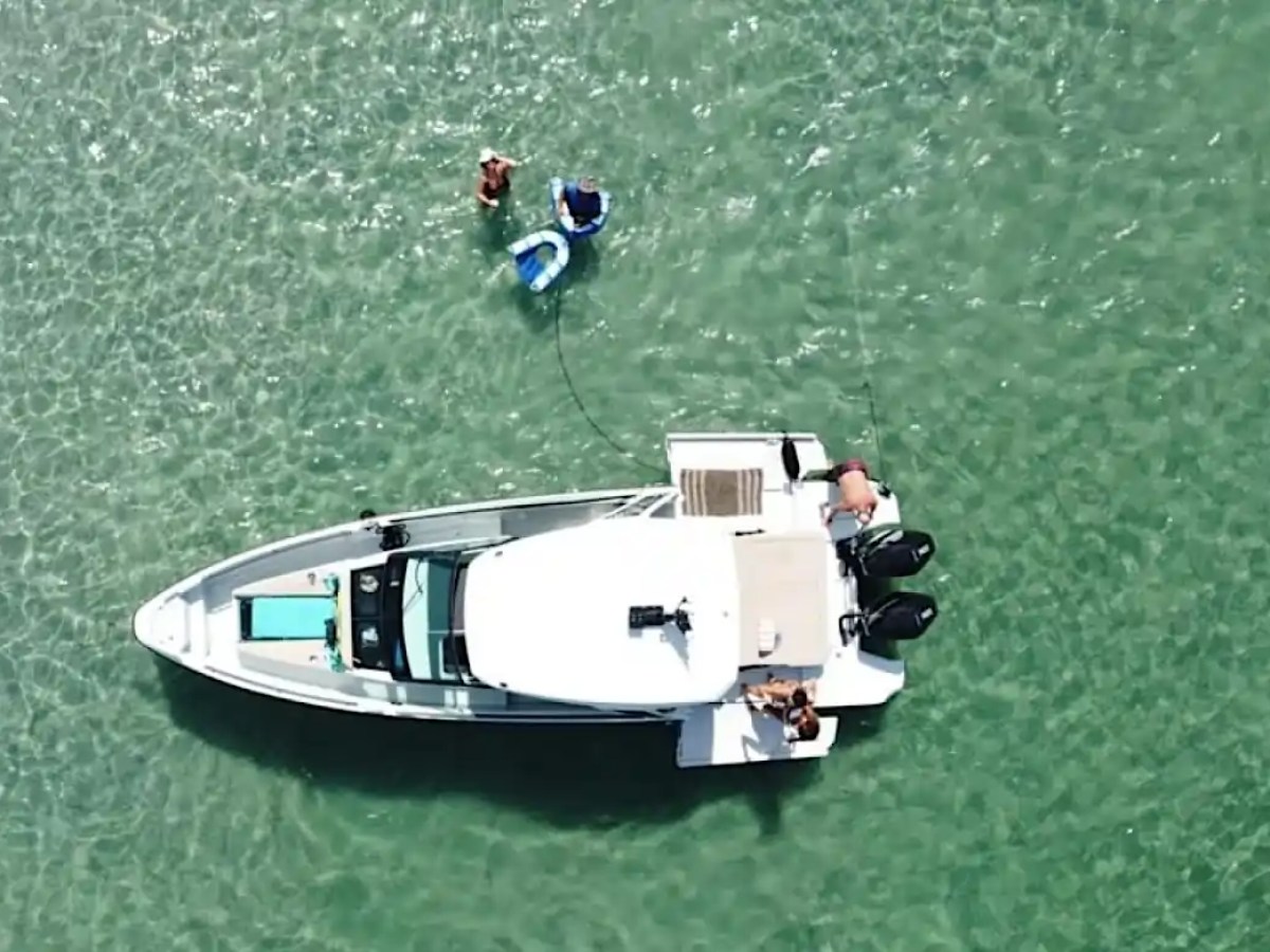 Aerial view of a boat on clear water with people swimming nearby.