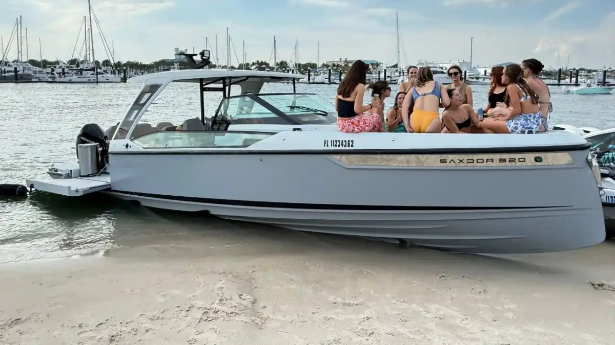 Group of people sitting on a beached boat near a marina on a sunny day.