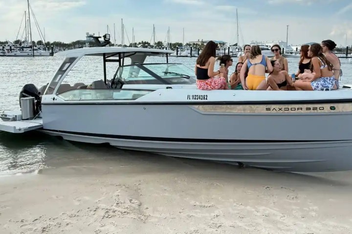 Group of people sitting on a beached boat near a marina on a sunny day.