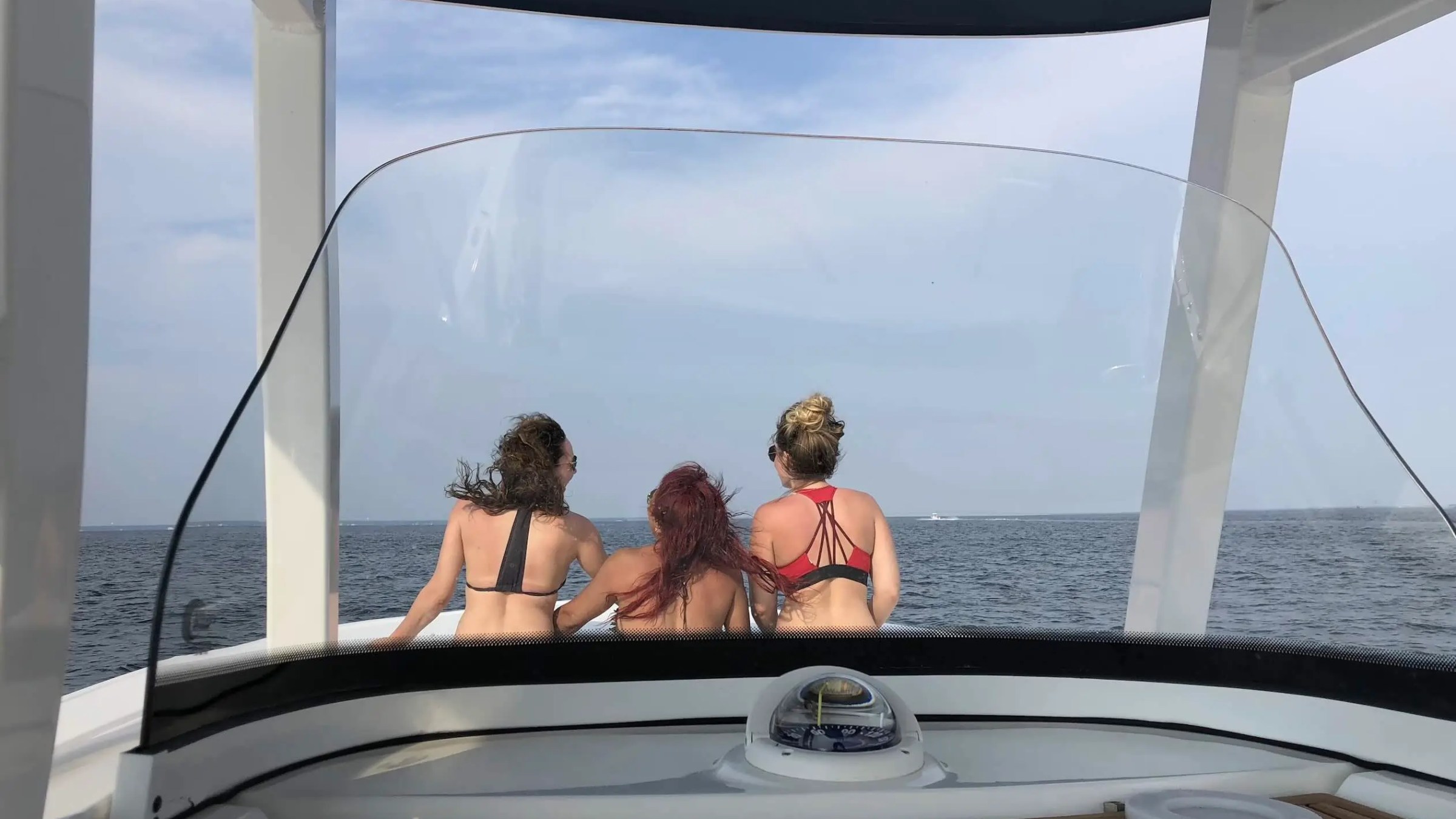 Three people in swimsuits sitting on a boat, facing the ocean.