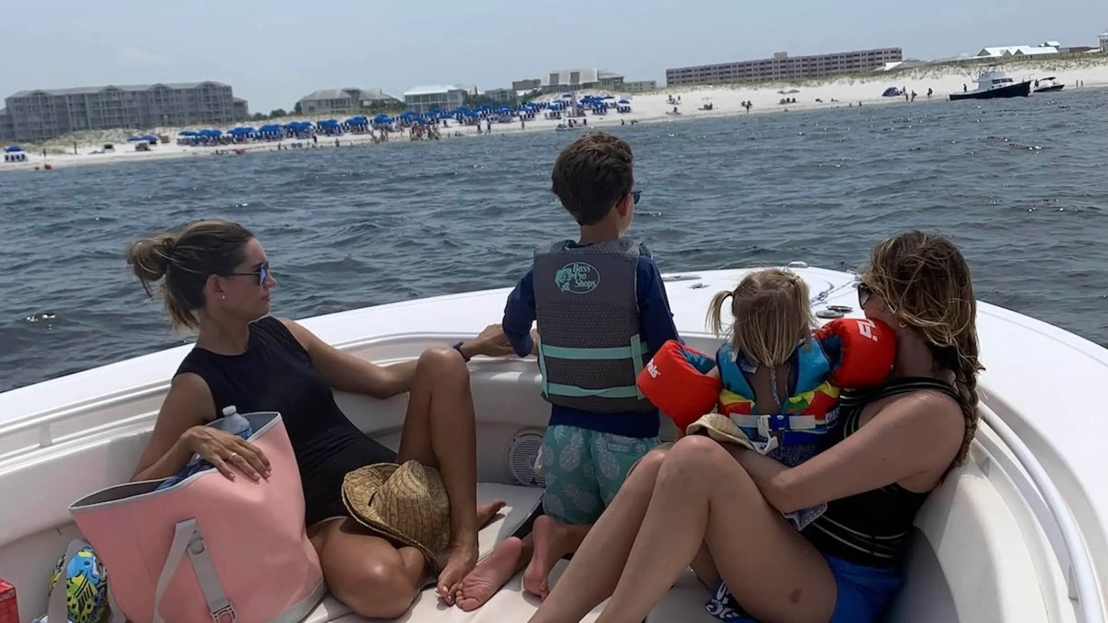Two adults and two children on a boat near a beach with umbrellas in the background.