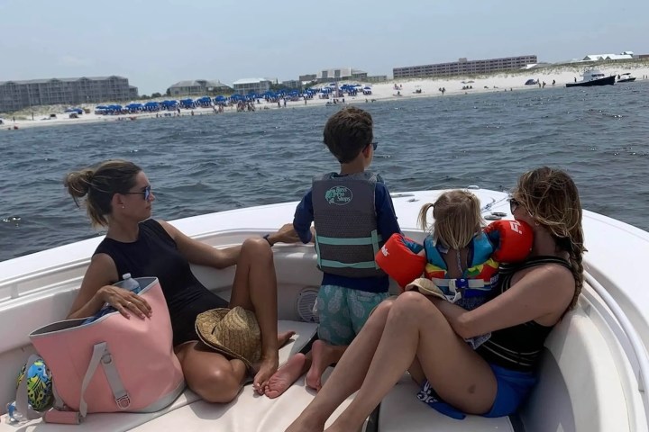 Two adults and two children on a boat near a beach with umbrellas in the background.