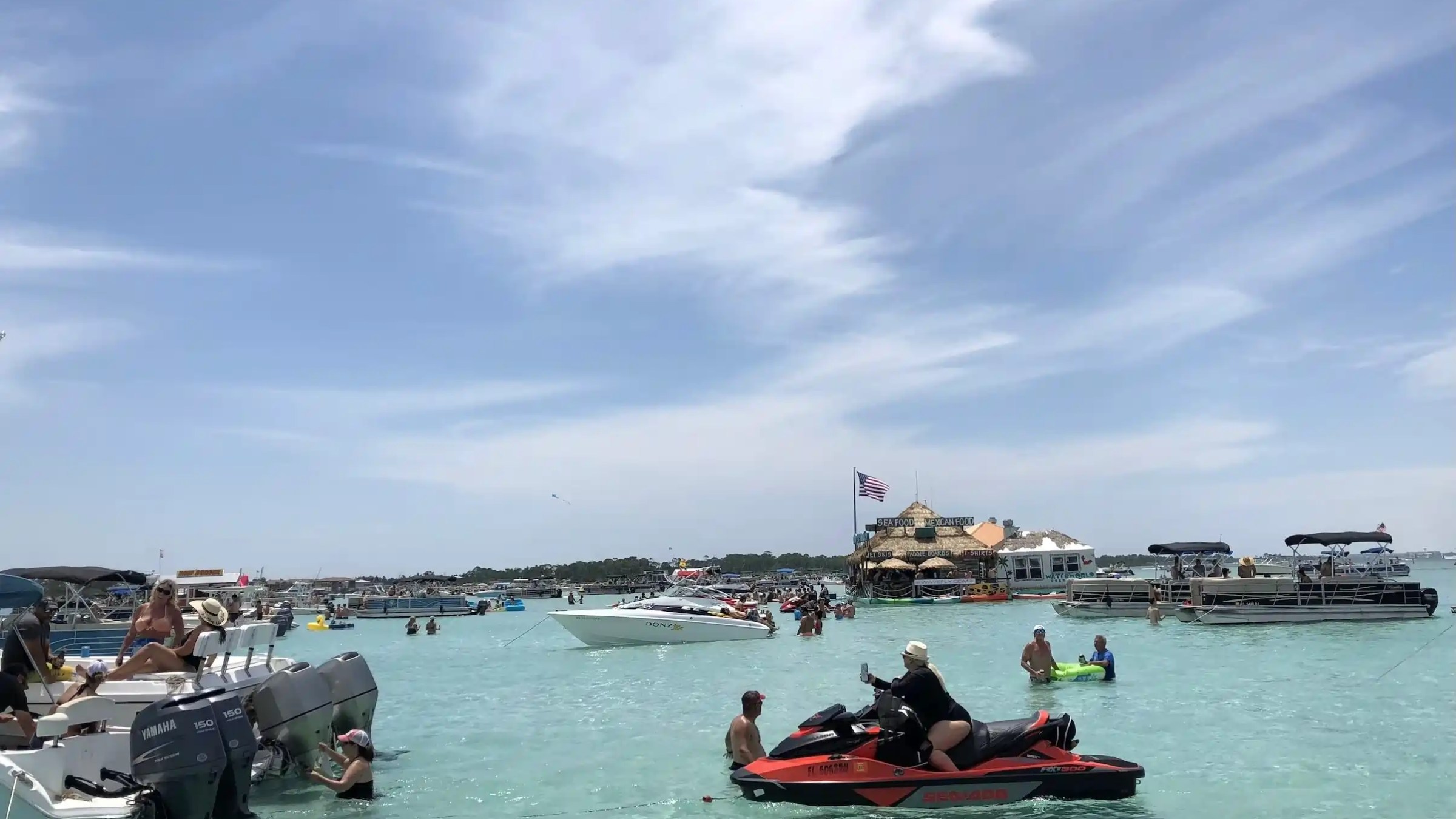 Boats and people in a clear lagoon with a floating structure in the background.