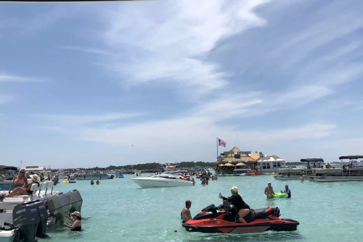 Boats and people in a clear lagoon with a floating structure in the background.