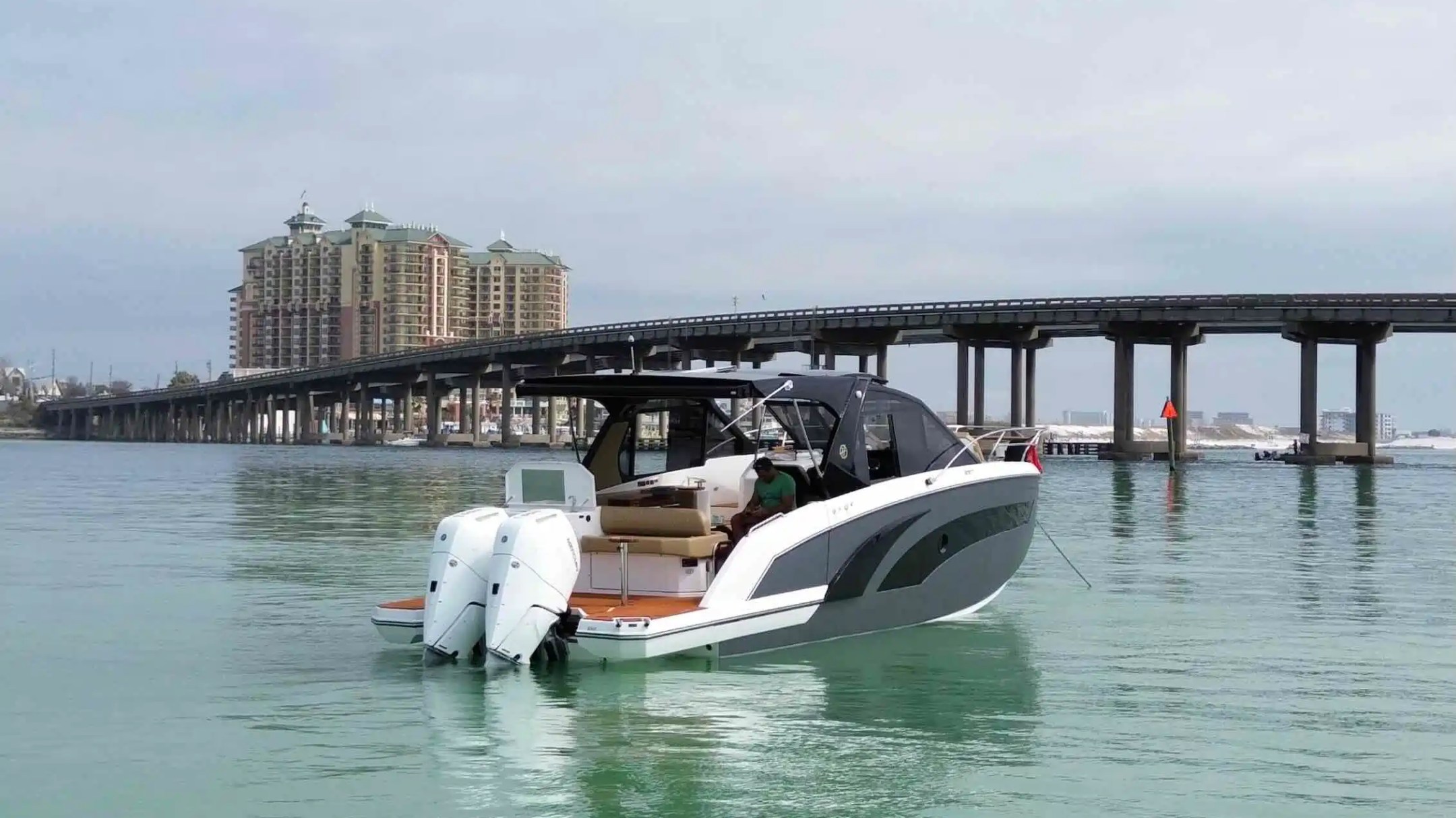 Motorboat on water near bridge with buildings in the background on a cloudy day.