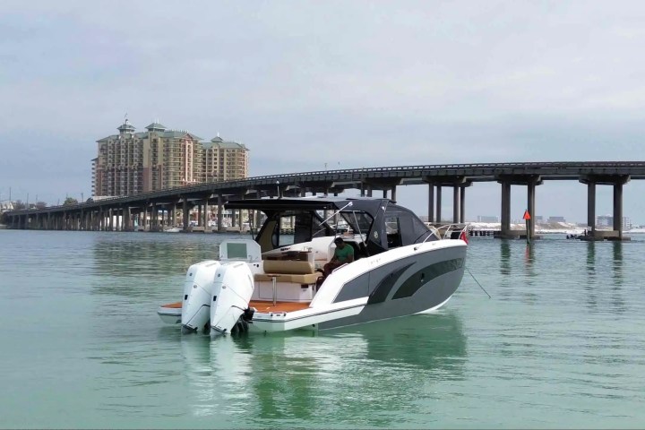 Motorboat on water near bridge with buildings in the background on a cloudy day.