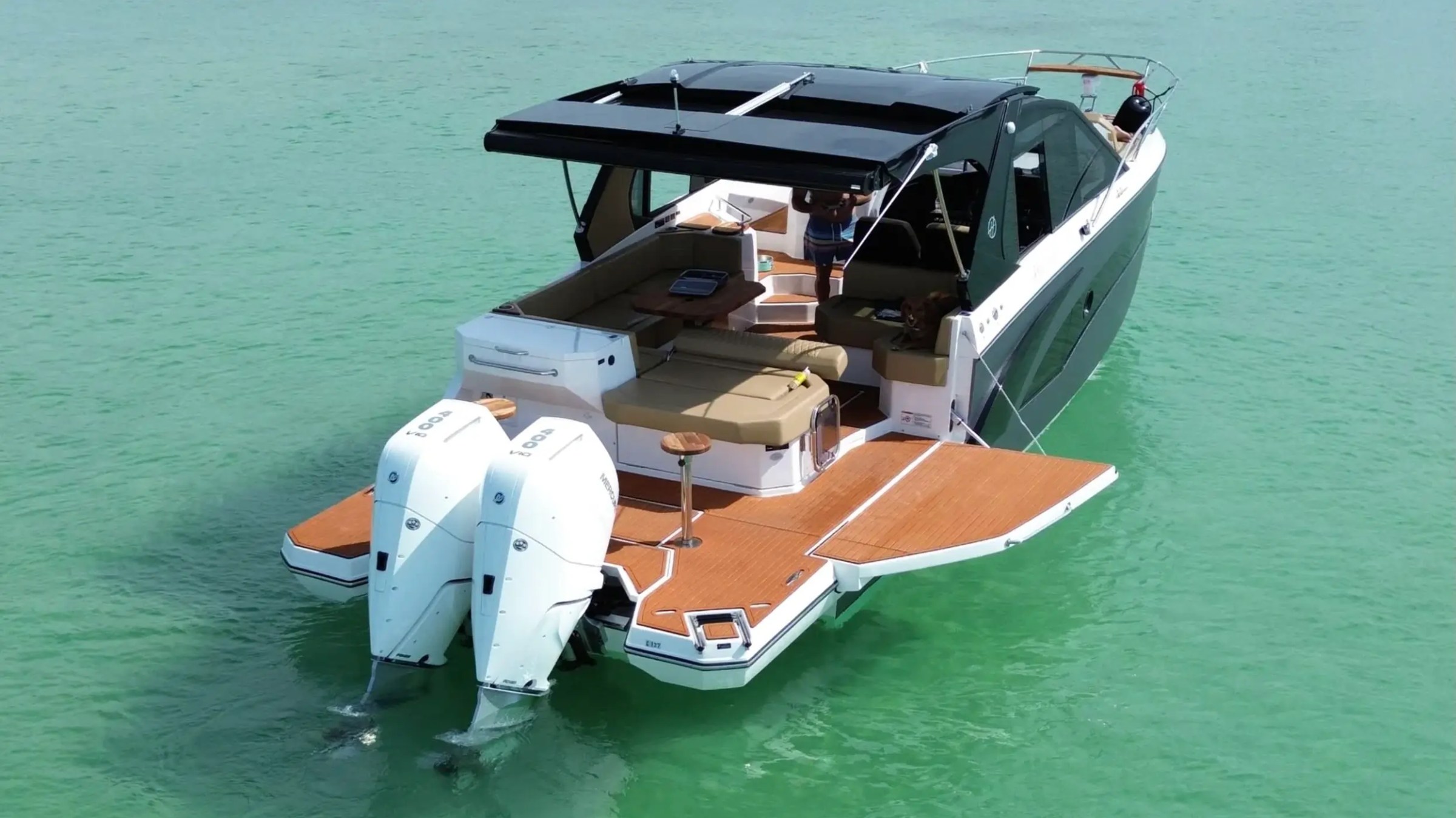 Luxury motorboat with dual outboard engines on calm green water.
