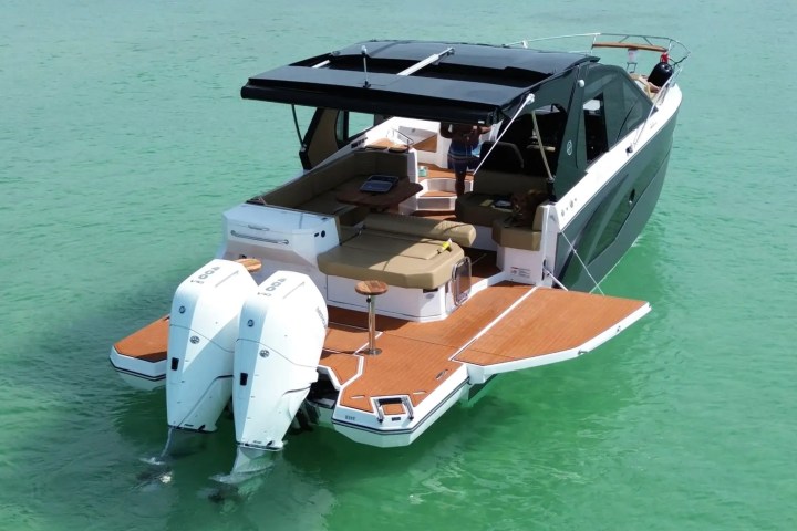 Luxury motorboat with dual outboard engines on calm green water.