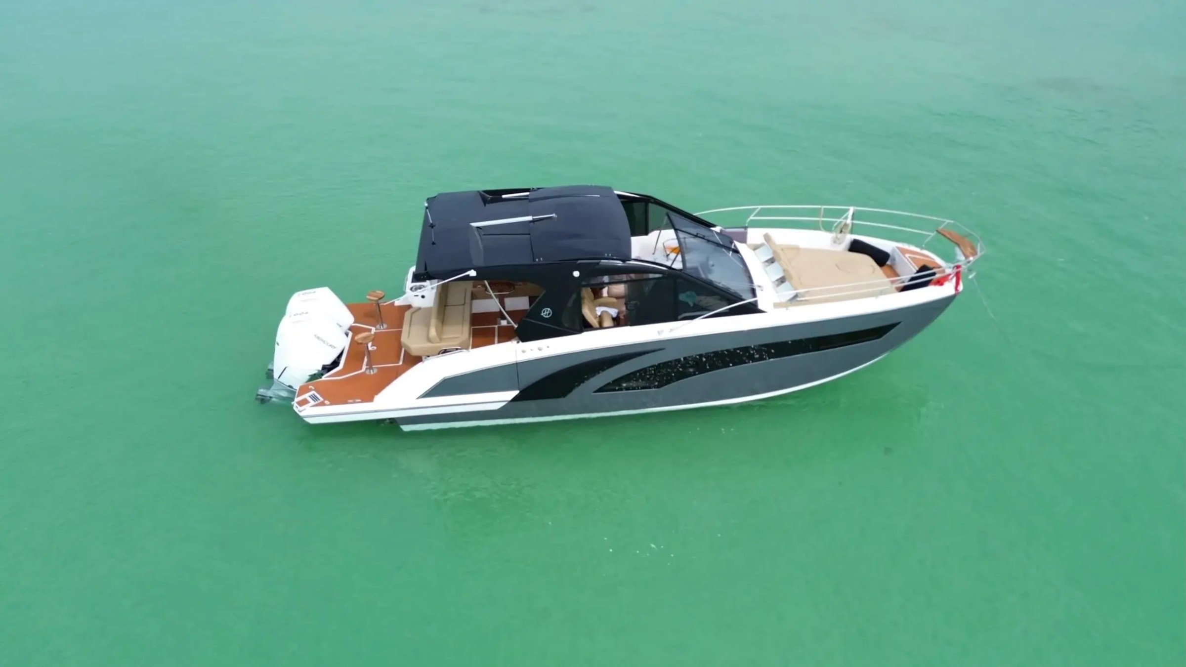 Motorboat with black canopy on turquoise water, aerial view.