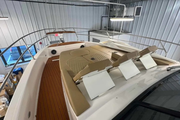 Interior view of a boat with tan seating and wooden deck, stored in a metal-walled warehouse.