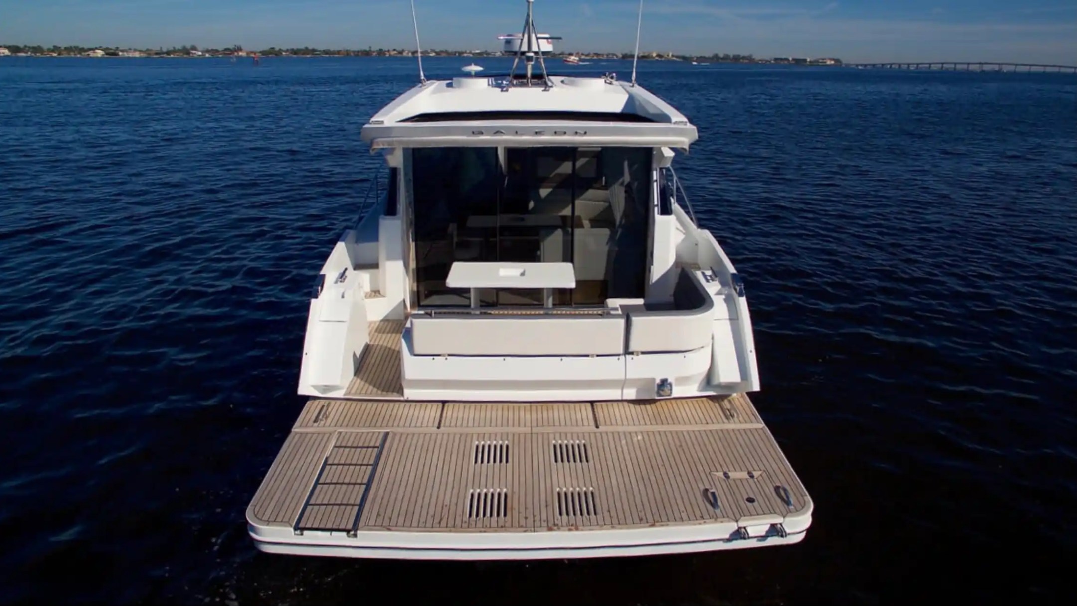 Back view of a modern yacht on calm blue water with distant shoreline.