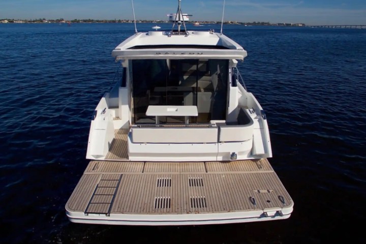 Back view of a modern yacht on calm blue water with distant shoreline.