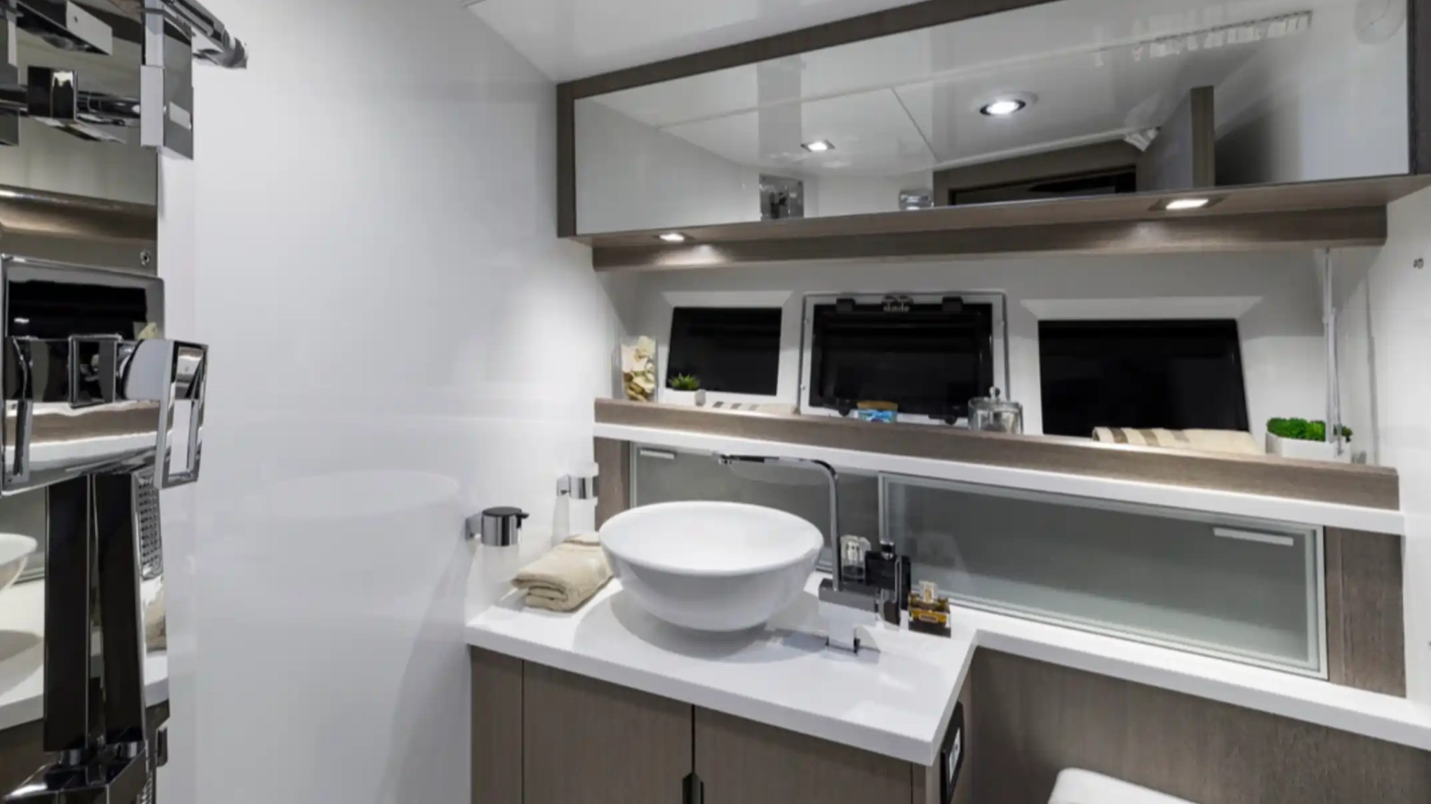 Modern bathroom with round sink, large mirror, and overhead spotlights on white and wood accents.