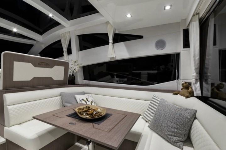 Elegant yacht interior with white seating, wooden table, and decorative pillows.