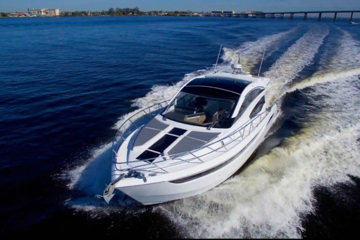 White yacht cruising on blue water with wake behind, clear sky and distant shoreline.