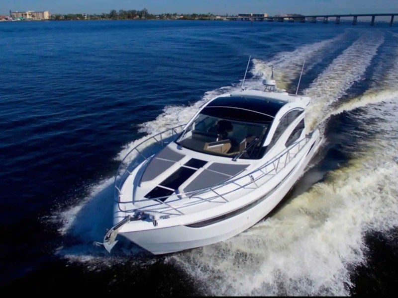 White yacht cruising on blue water with wake behind, clear sky and distant shoreline.