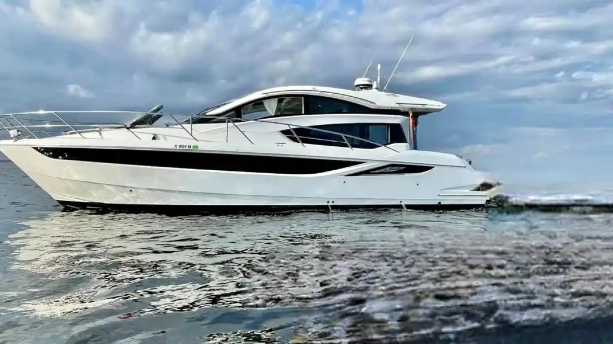 A white yacht floating on calm water under a cloudy sky.