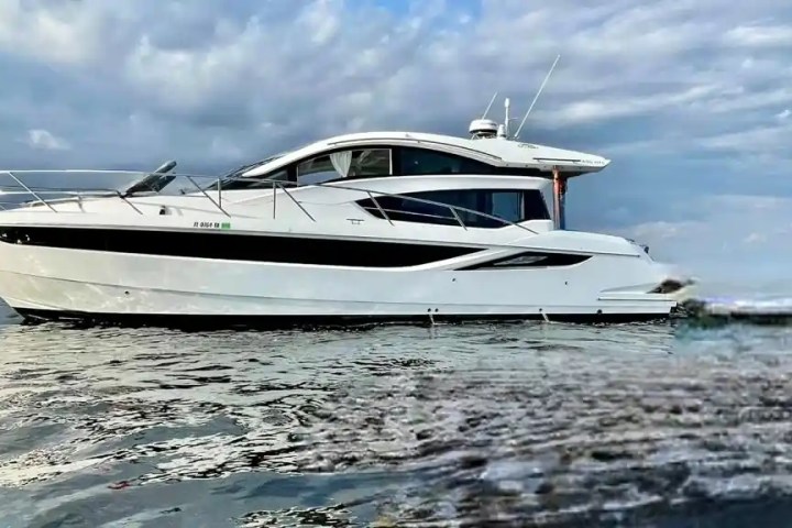 A white yacht floating on calm water under a cloudy sky.