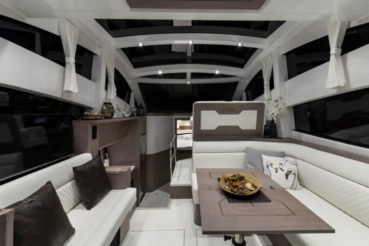 Modern yacht interior with white sofas, brown table, decorative pillows, and large windows.