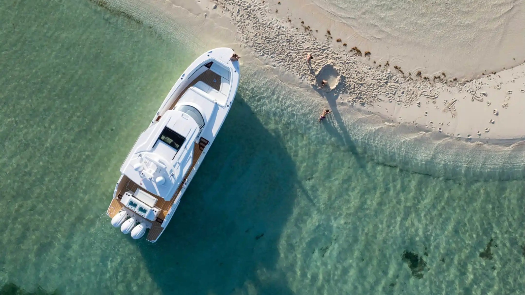 Aerial view of a white boat docked on clear water near a sandy beach.
