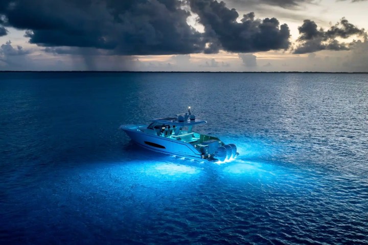 Boat with blue underwater lights on a calm ocean under a dramatic cloudy sky.