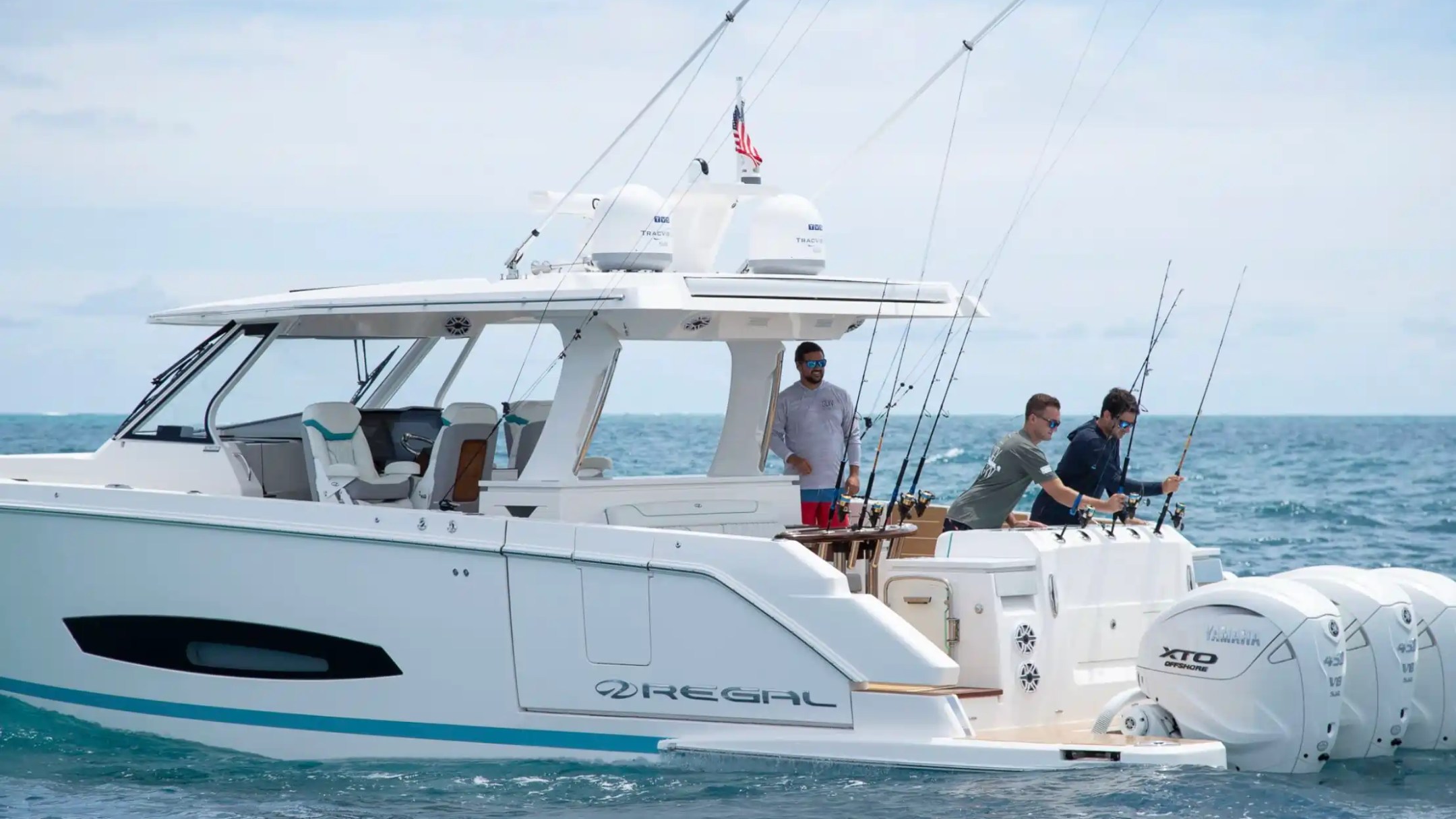 Three people fishing on a white boat in the ocean with a clear sky.