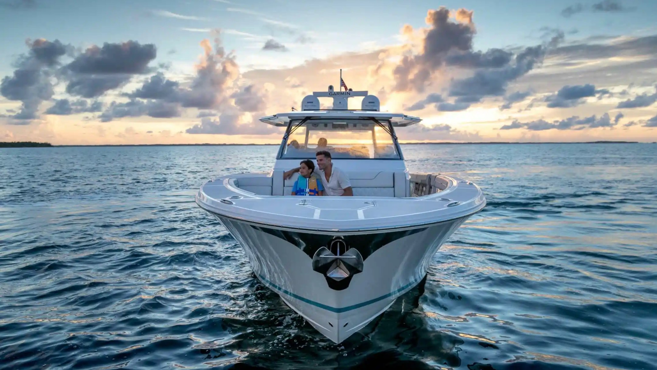 People sitting on a boat in the ocean at sunset with cloudy sky.