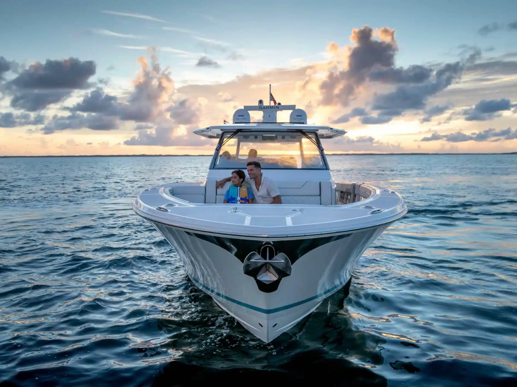 People sitting on a boat in the ocean at sunset with cloudy sky.