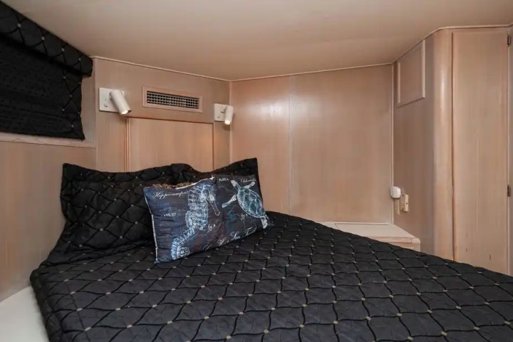 Small cozy bed with black quilted bedding and seahorse pillow in a compact, wood-paneled room.